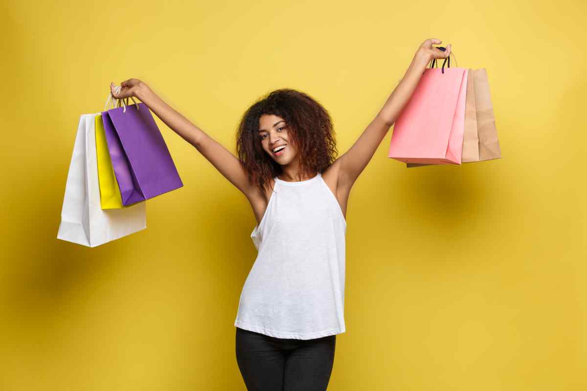 shopping concept close up portrait young beautiful attractive african woman smiling joyful with colorful shopping bag yellow pastel wall background copy space